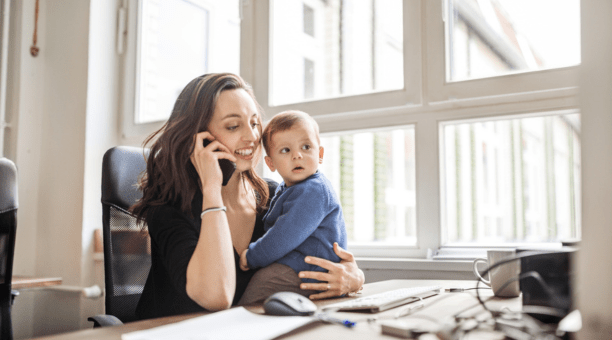 Career woman on phone at work while holding her baby who sits on her desk.