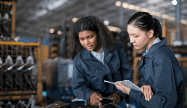 Two women wearing navy jackets looking down at a machine.