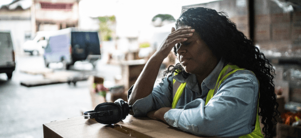 Stressed warehouse worker with her hands to her forehead.