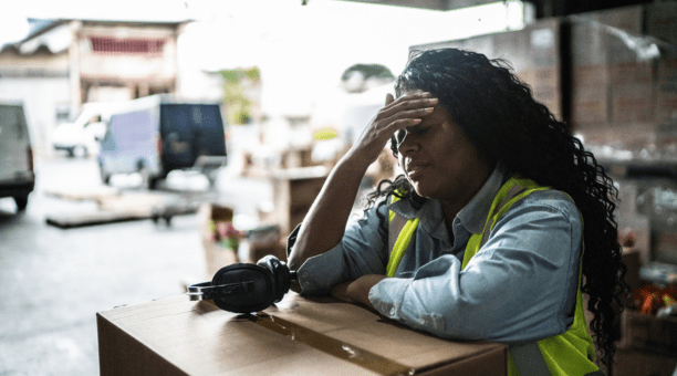 Stressed warehouse worker with her hands to her forehead.