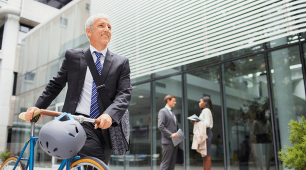 Man bikes to work with other professionals behind him in front of office building.