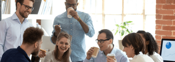 Diverse group of coworkers drinking coffee and laughing while working at a conference table.