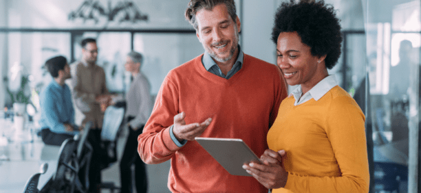 Man and woman looking at tablet in office smiling.