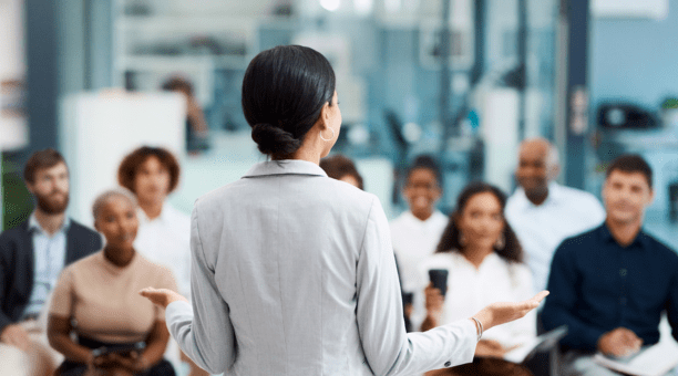 Back of woman as she speaks to a group of employees about benefits.