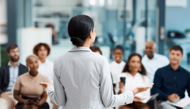 Back of woman as she speaks to a group of employees about benefits.
