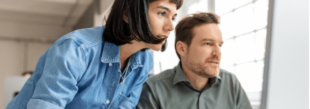 Male and female employees looking at a computer together.