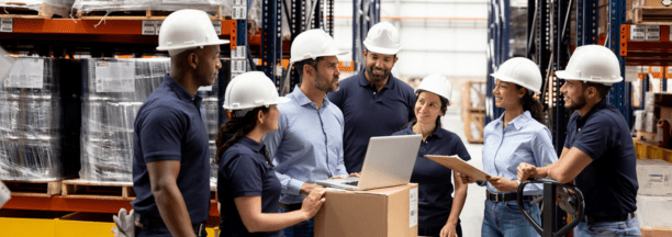 Group of employees wearing hard hats talking in a warehouse.
