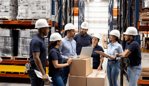 Group of employees wearing hard hats talking in a warehouse.