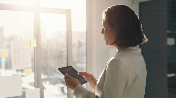 Woman holding a tablet looking out a window.